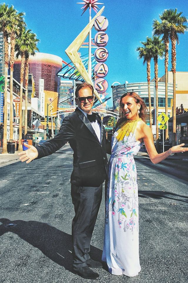 Marc Mulvaney in a tuxedo with a woman in a long floral dress under the Vegas neon sign in downtown Las Vegas