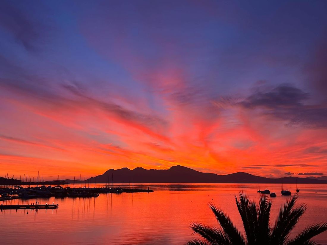 Red sky over the bay of Port de Pollença, Mallorca, with the marina, moored boats and mountains in silhouette