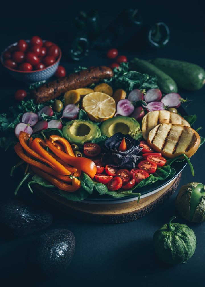 Vegan salad bowl with avocado, cherry tomatoes, radishes, orange pepper and a grilled vegan sausage on a dark table